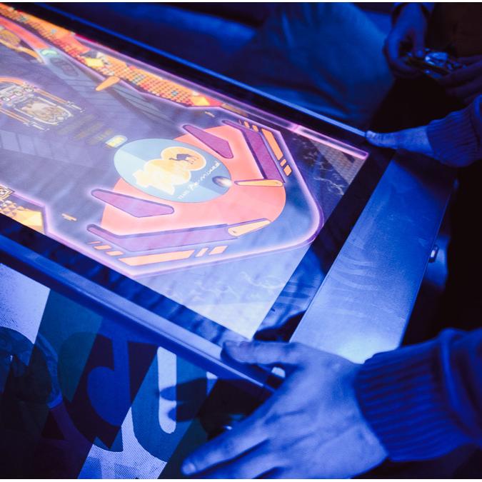 A player engages with a digital pinball machine featuring a Camel brand theme, illuminated in blue.