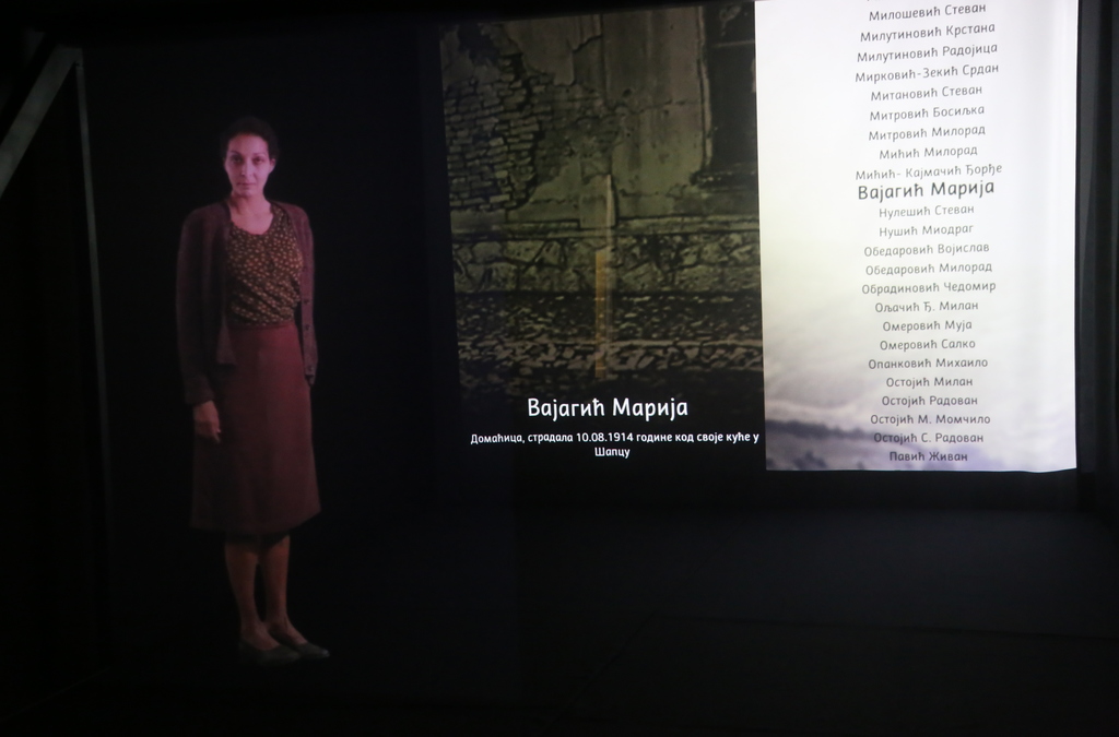 A holographic representation of a WWI female victim stands next to a projection of names and historical context.