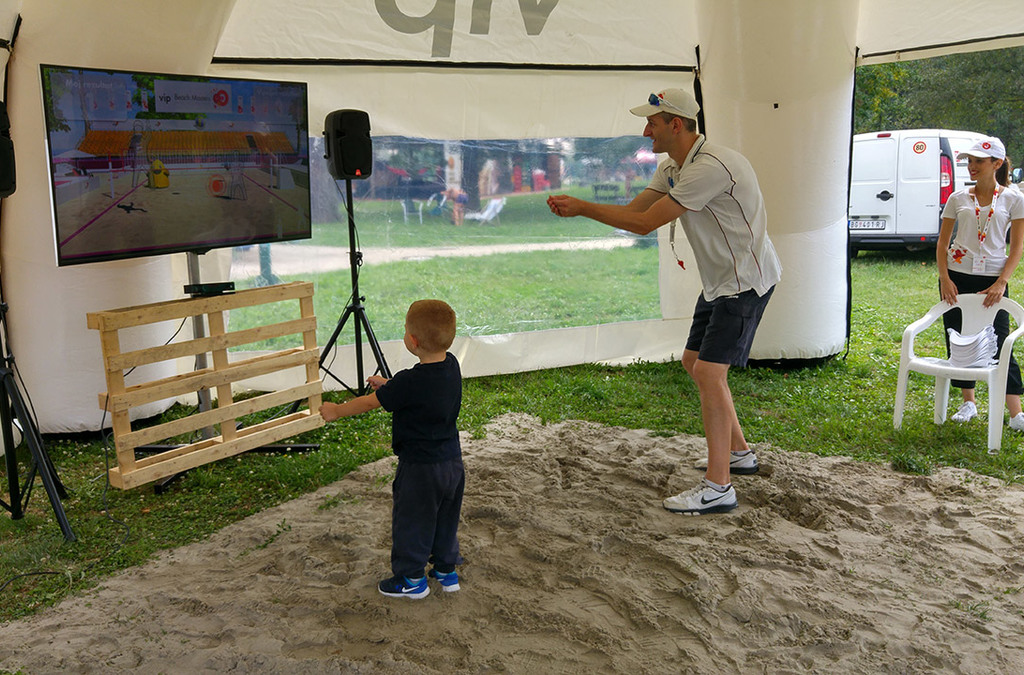 An adult and a small child play Kinect volleyball at an interactive installation sponsored by VIP Mobile, with no physical controllers needed.