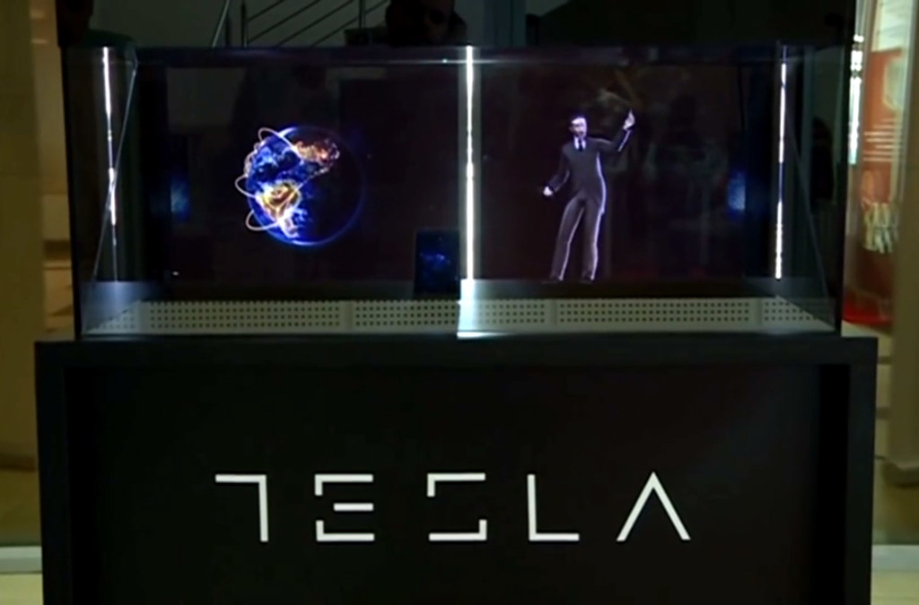 A display case with the Tesla logo illuminates a holographic projection of Nikola Tesla. The exhibit is designed to promote the new Tesla smartphone, symbolizing the fusion of technology and Tesla's scientific legacy.