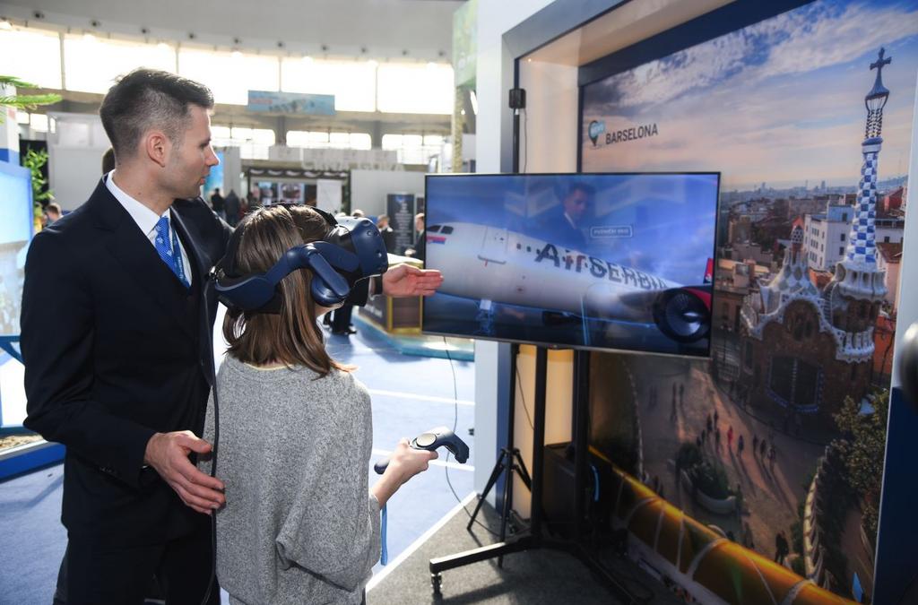 A woman wearing a VR headset is guided by an Air Serbia representative to explore a virtual aircraft.