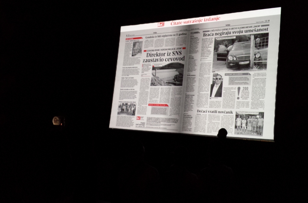 A silhouette of a person flipping through a projected digital newspaper page using hand movements detected by Microsoft Kinect technology in a low-lit setting.