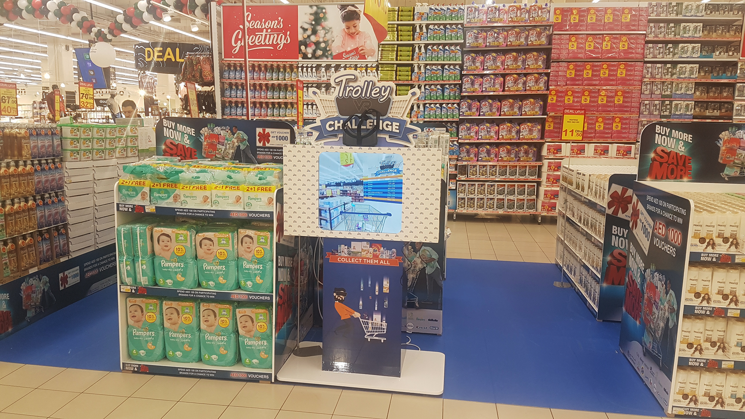 A promotional stand for 'VR Trolley Challenge' situated in a bustling Carrefour store. The stand features vibrant signage and a screen showing a virtual shopping basket. Products and special offers are displayed around the area.