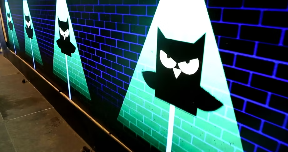 A close-up of a part of an interactive gaming installation, showing projected images of an owl character on pyramid-shaped markers against a brick wall, with a blue digital background.