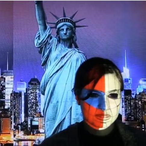 Two people participate in a real-time face mapping installation, with projections of New York City and the Statue of Liberty on their faces.