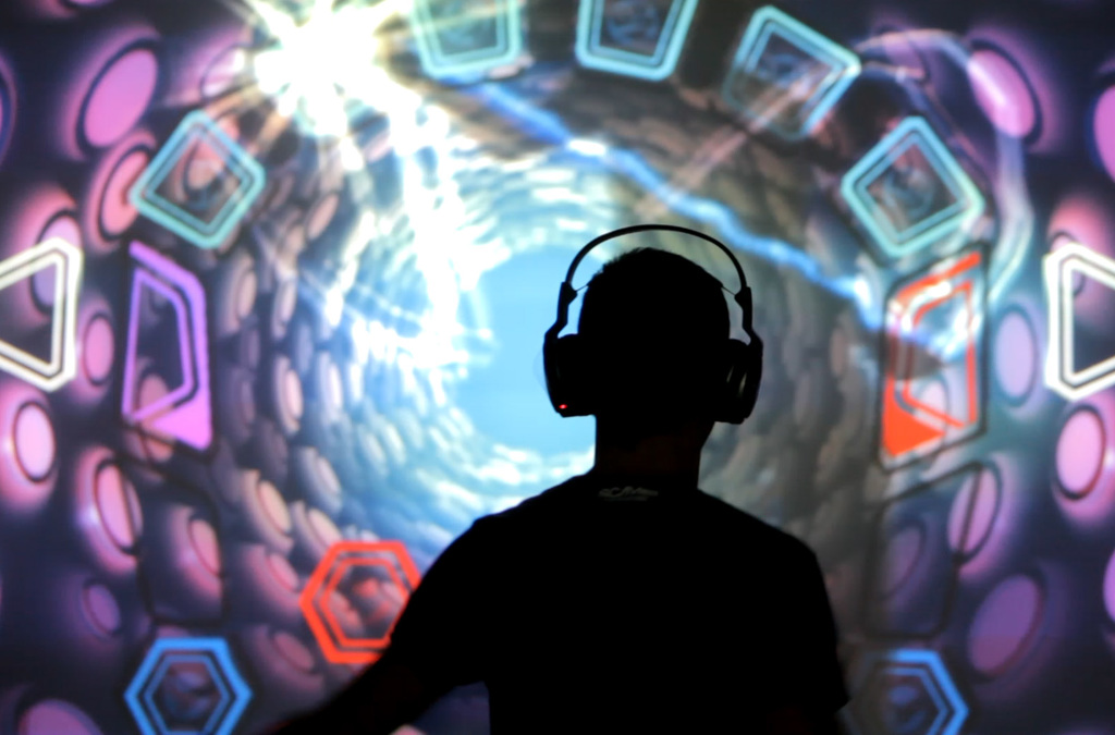Silhouetted against a mesmerizing backdrop of a luminous virtual vortex, a person with headphones orchestrates music and visual effects with the motion of their body in an interactive VJDJ environment.