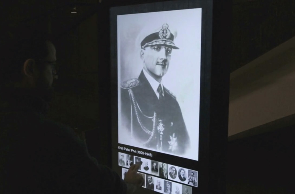 A visitor at the Museum of Yugoslav History interacts with a digital totem, selecting an image of King Alexander I of Yugoslavia from the historical figures displayed.
