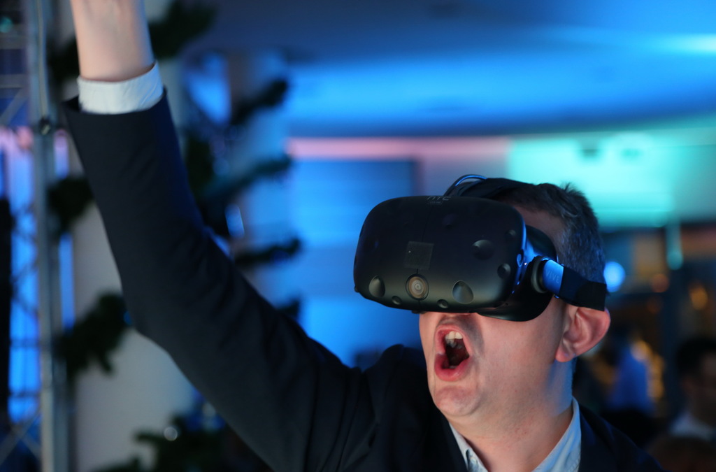 A man wearing a VR headset is caught in an expressive moment, arm raised high as if shooting a basketball in a virtual game.