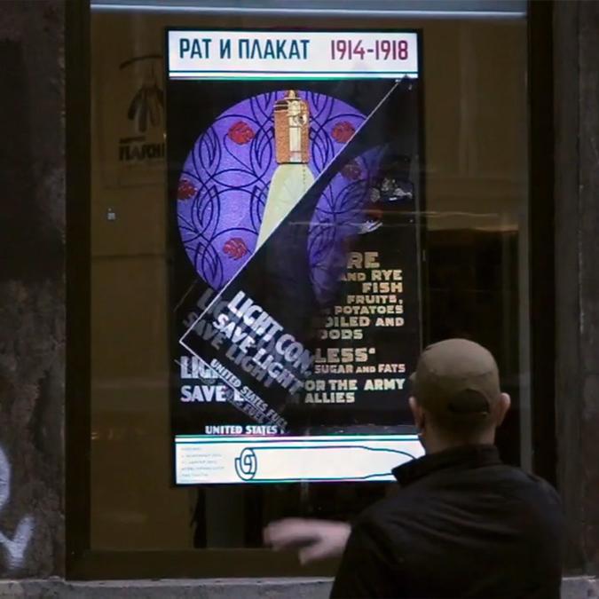 A man interacts with an interactive screen displaying a vintage war poster as part of the “Rat i Plakat” exhibition on the street.