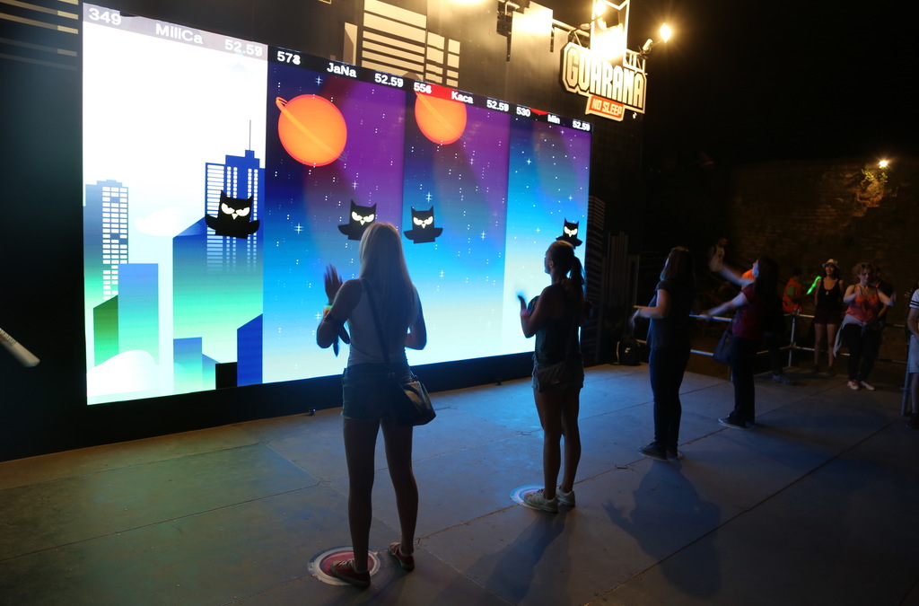Participants focused on playing an interactive game at an event, standing in front of a large LED screen displaying an owl, part of a Guarana promotion.