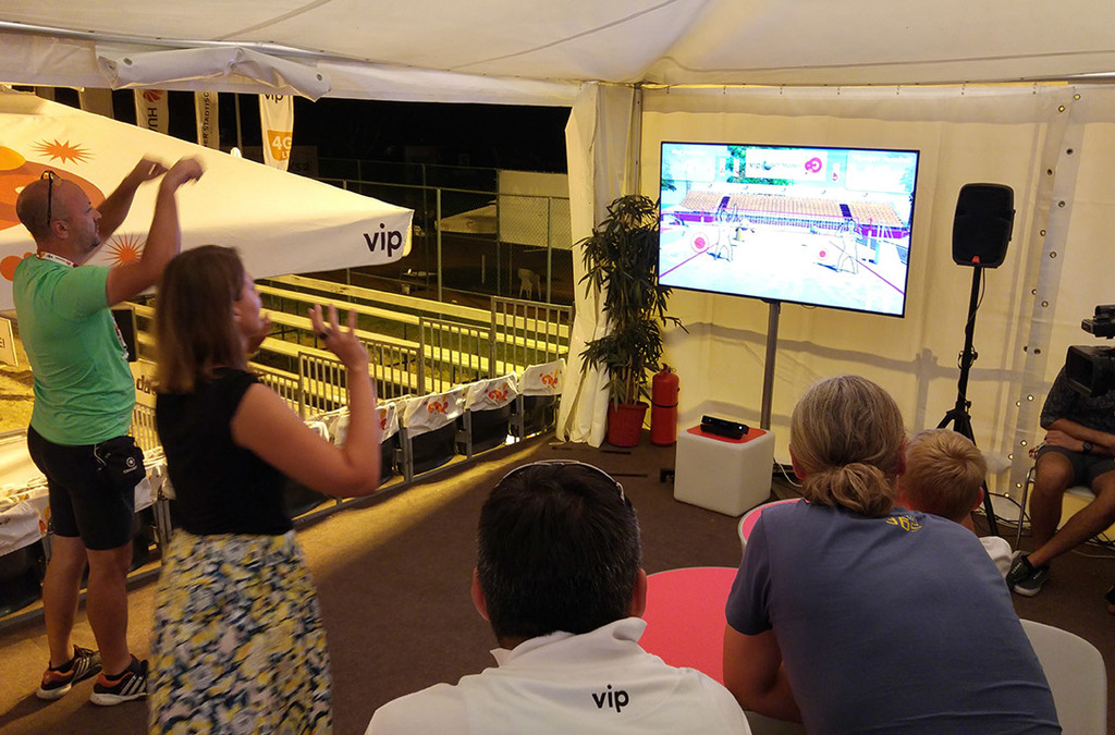 Spectators watch as participants play Kinect volleyball at a VIP Mobile-sponsored event, interacting with the game using body movements.