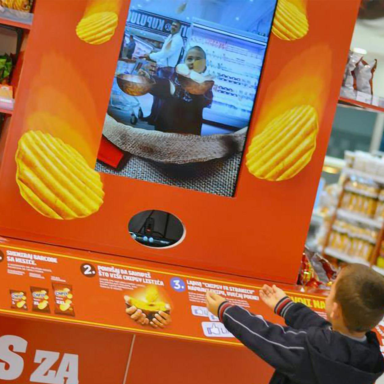 A young boy engaging with the Chipsy AR game, attempting to catch virtual chips projected on a screen in a supermarket setting.