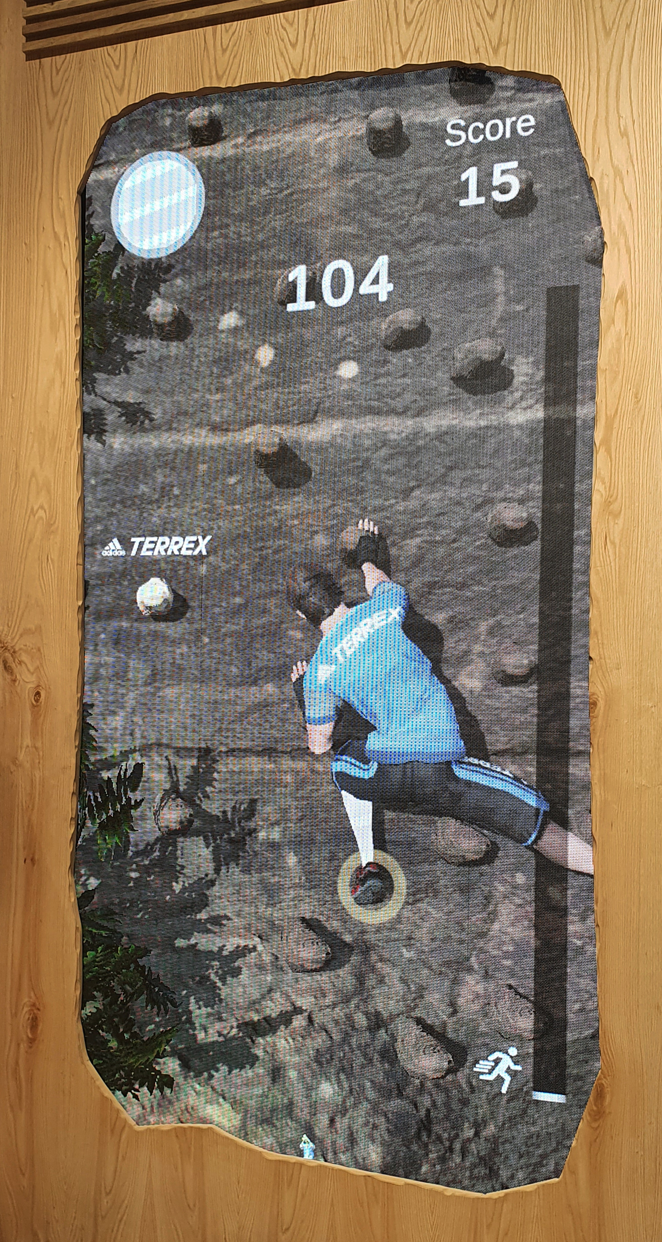Close-up view of the 'Sport Vision Climbing' game screen, which shows a score and time counter. A virtual climber is seen ascending a digital rocky cliff, representing the player's movements in the interactive game.