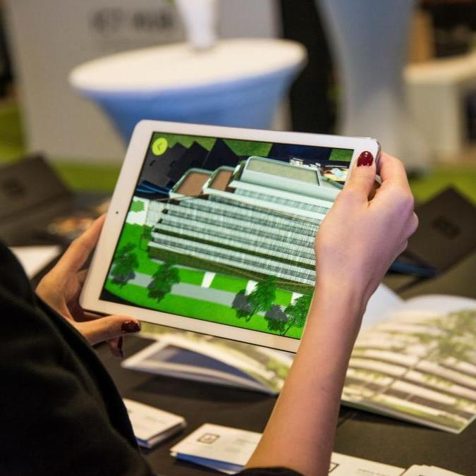 Close-up of a person holding an iPad displaying an augmented reality (AR) model of the GTC Green Heart Complex, overlaid on a physical brochure with the layout of the complex, demonstrating the innovative way of exploring real estate through AR technology.