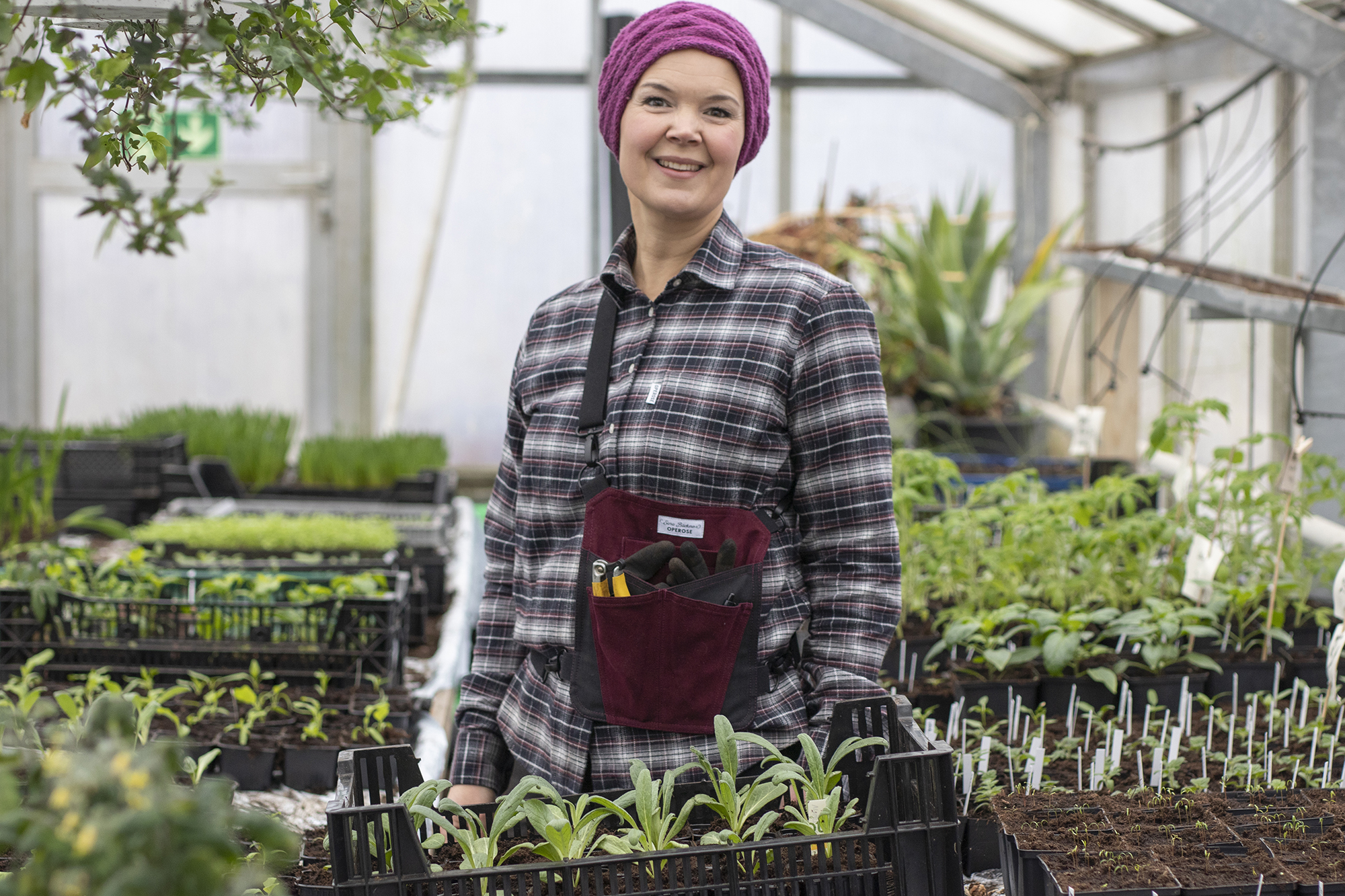 Sara Bäckmo står bland plantor och bär en vinröd trädgårdsväska