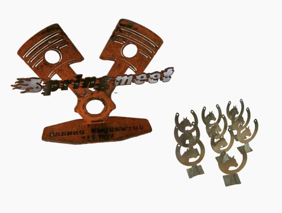 Till vänster en prispokal tillverkad i Corten och rostfritt stål, till höger små priser pulverlackerade i guld-candy.