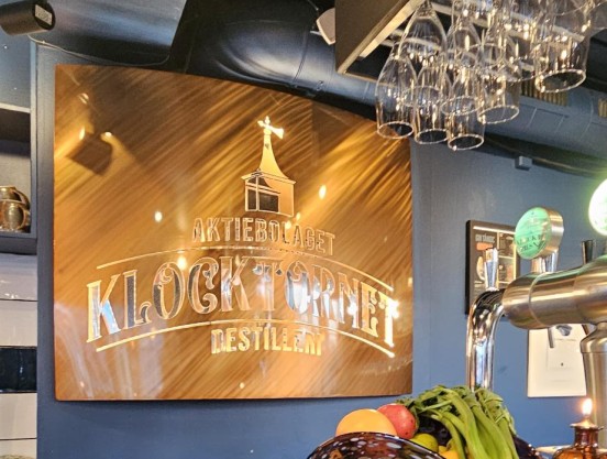 Bild på belyst välvd skylt med utskuren logga och slipad fishish, pulverlackerad i coppar-candy.