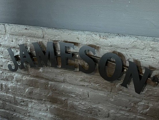 Loggoskylt i forma av mattsvarta profilbokstäver på en bågformad profil, monterad frampå en bardisk.