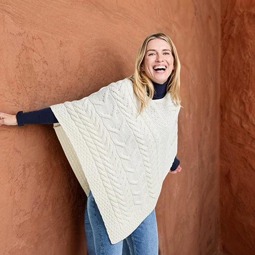 Kvinna med stickad vit mjuk poncho i 100% merinoull