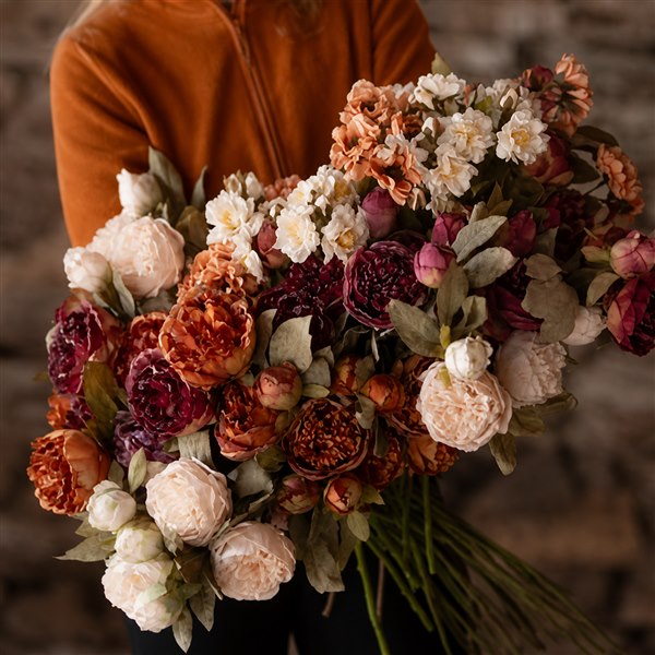 Fyllig bukett med konstblommor i aprikos, vinrött och crème i en varm inomhusmiljö
