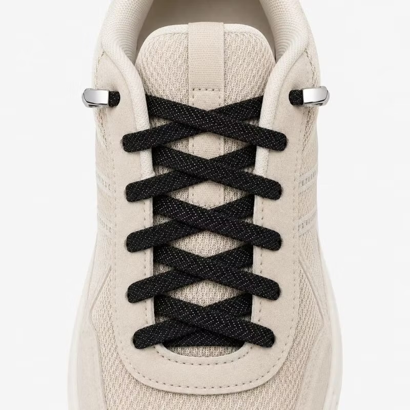 Svarta elastiska skosnören med platta metallfästen på en beige sneaker.