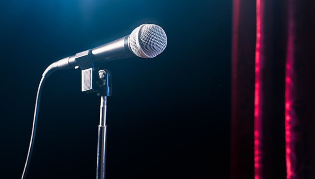 Silver microphone in front of a black background with a red curtain at the side