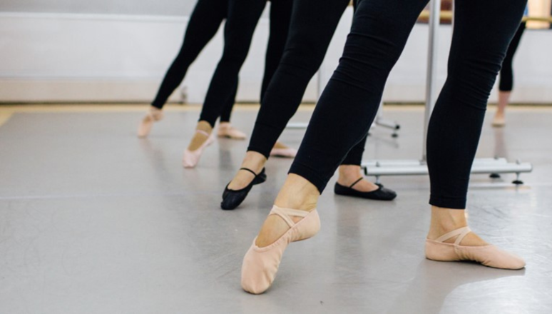 Ballet dancers stood at the bar, close of their feet in ballet shoes, pointing their toes