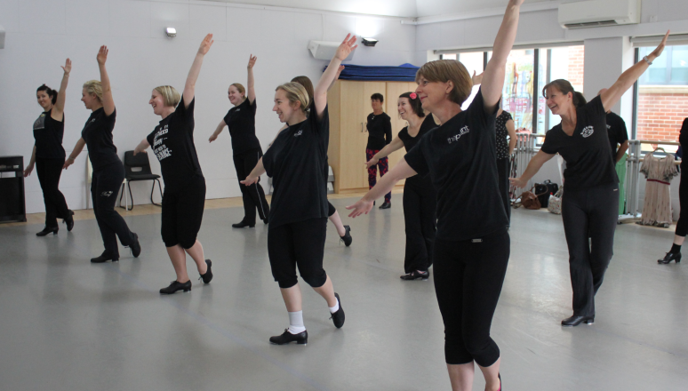 Group of dancers in the Dance Studio wearing tap shoes and posing with their arms out