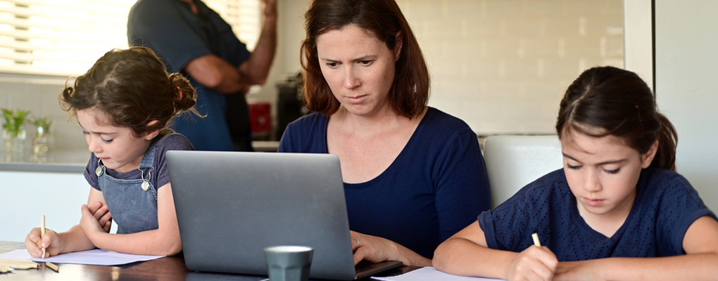 Mutter sitzt mit ihren beiden lernenden Kindern am Tisch und schaut auf den Laptop