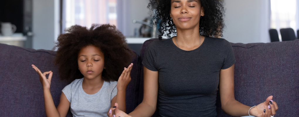 Eine Mutter und ihre Tochter sitzen in einer Yoga-Pose auf einer Couch