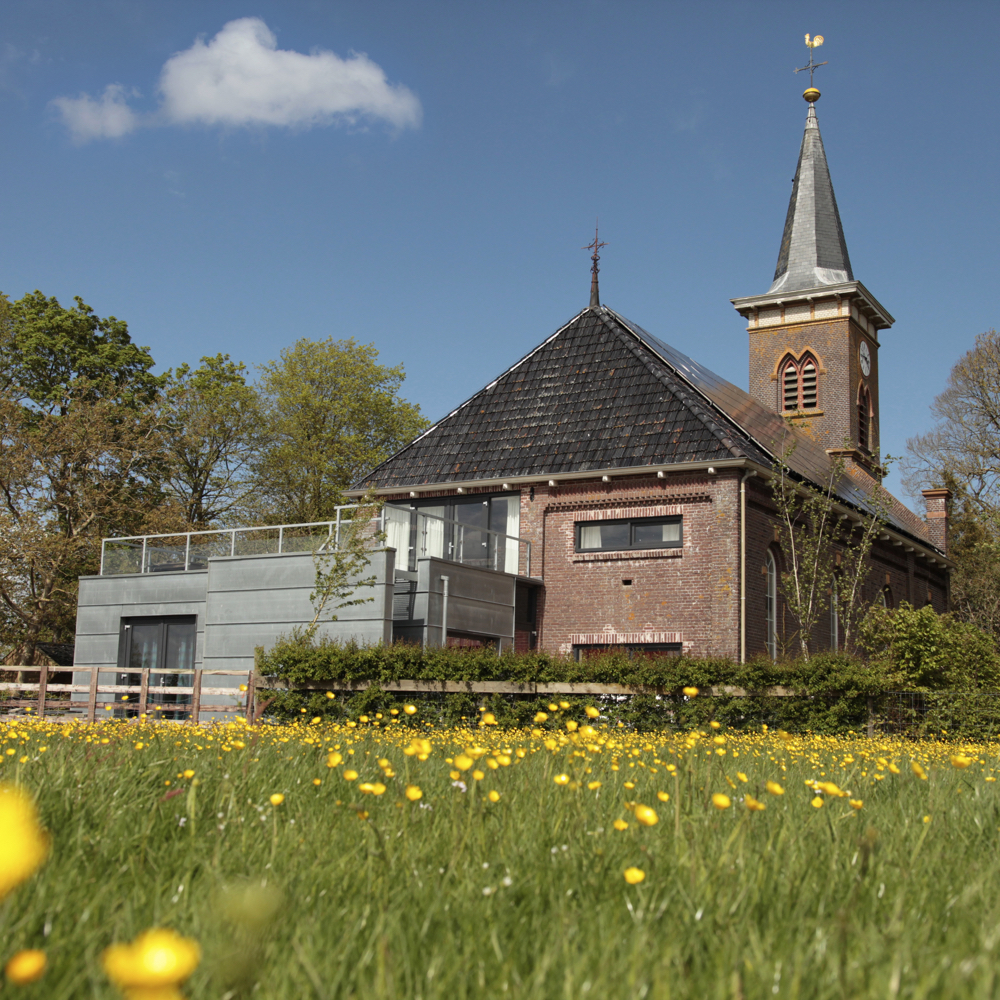Een vakantiehuisje in de weide met een kerk op de achtergrond