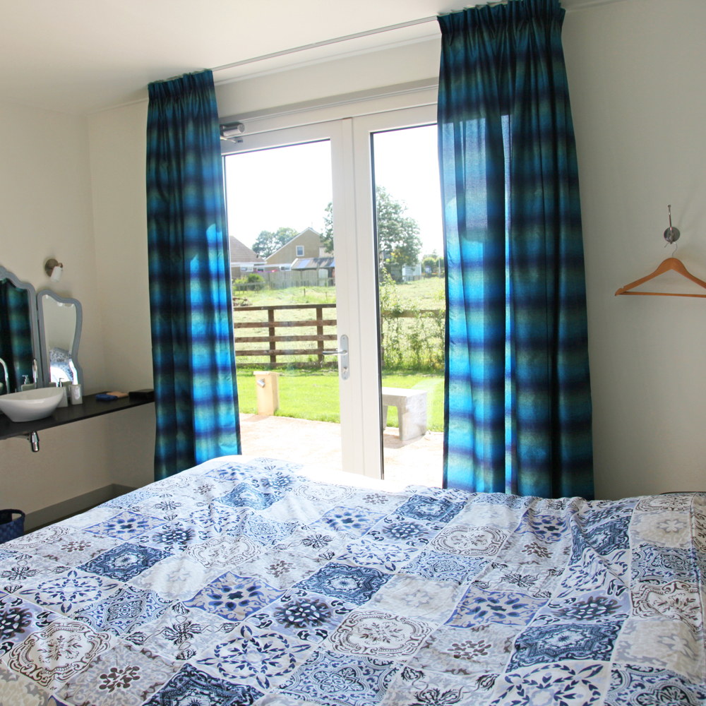 Bed met blauwe dekens met een deur dat uitzicht toont op de weides