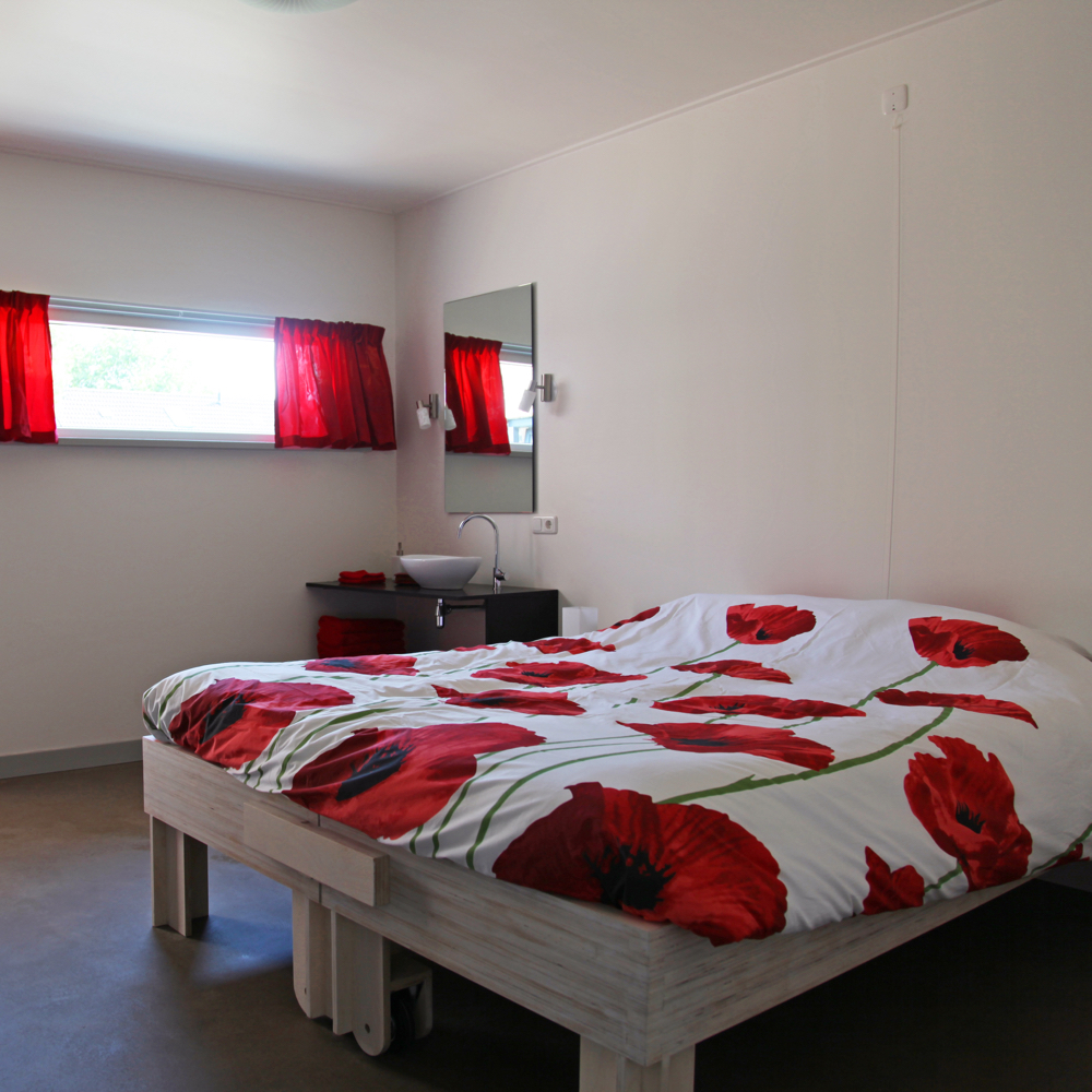 Bed met deken waarop rozen staan. Naast het bed staat een wastafel