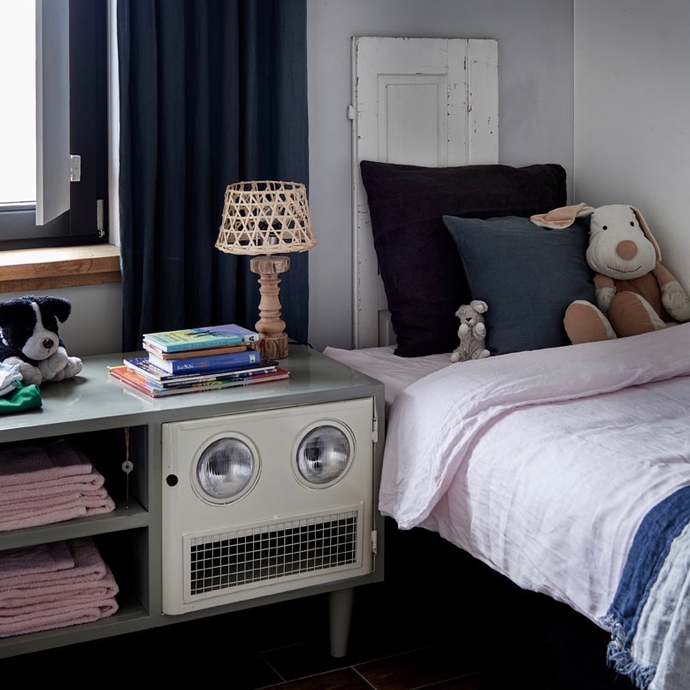 Bed met kussens en knuffels, nachtkastje met stapel kinderboeken en nachtlampje