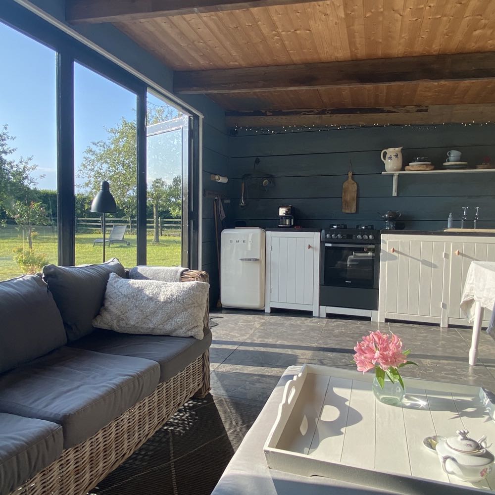 Midden in de boomgaard staat de tuinkamer, met een buitenkeuken, houtkachel en loungebanken.