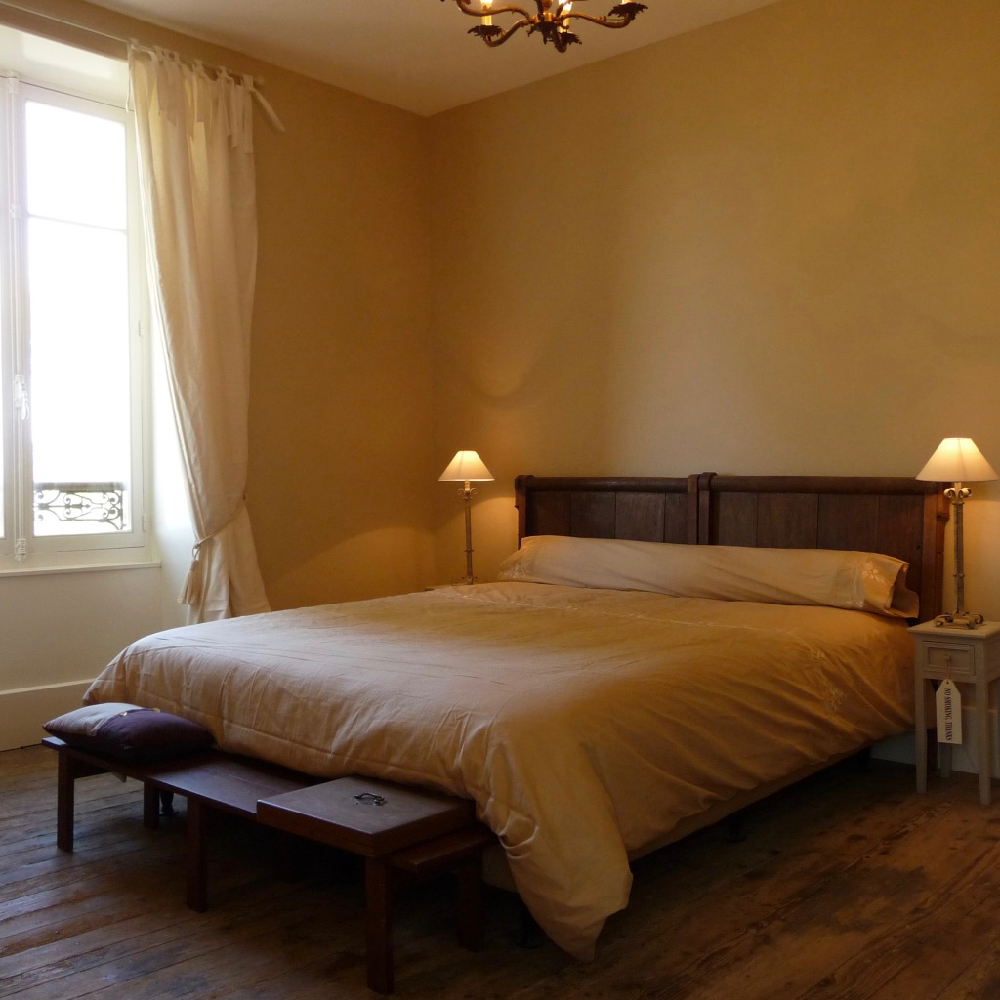 Tweepersoons bed met houten achterwand en schemerlampjes op de nachtkastjes