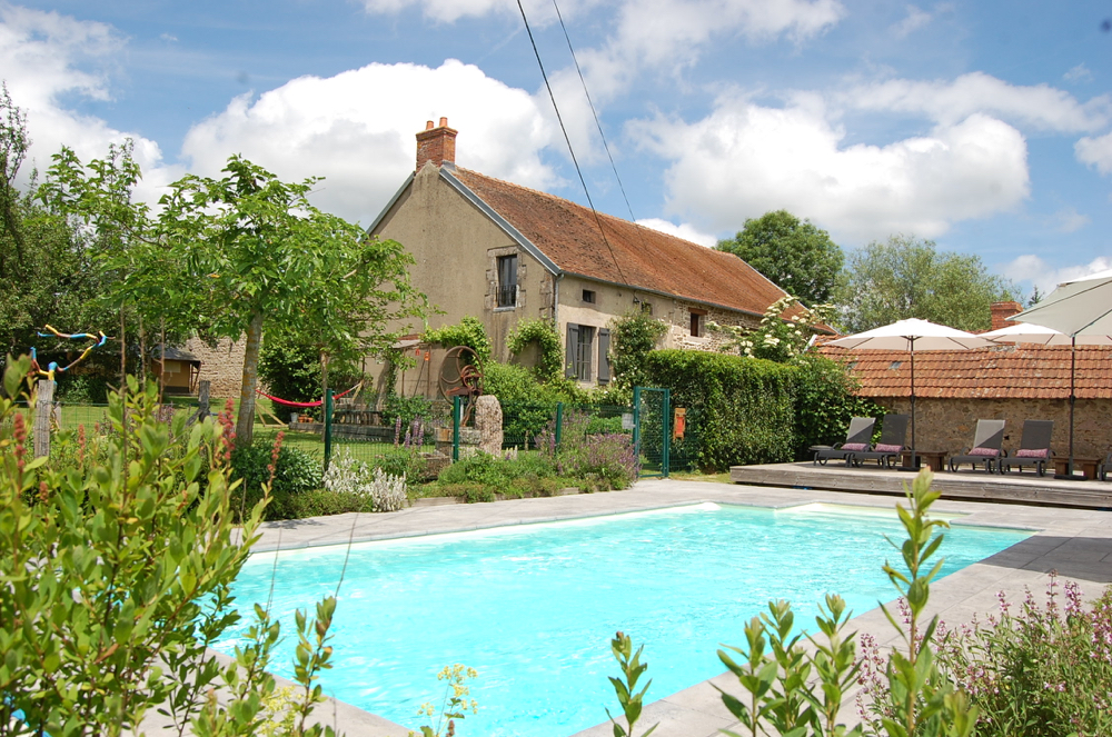 Zwembad met ligstoelen, parasols en Franse boerderij ernaast