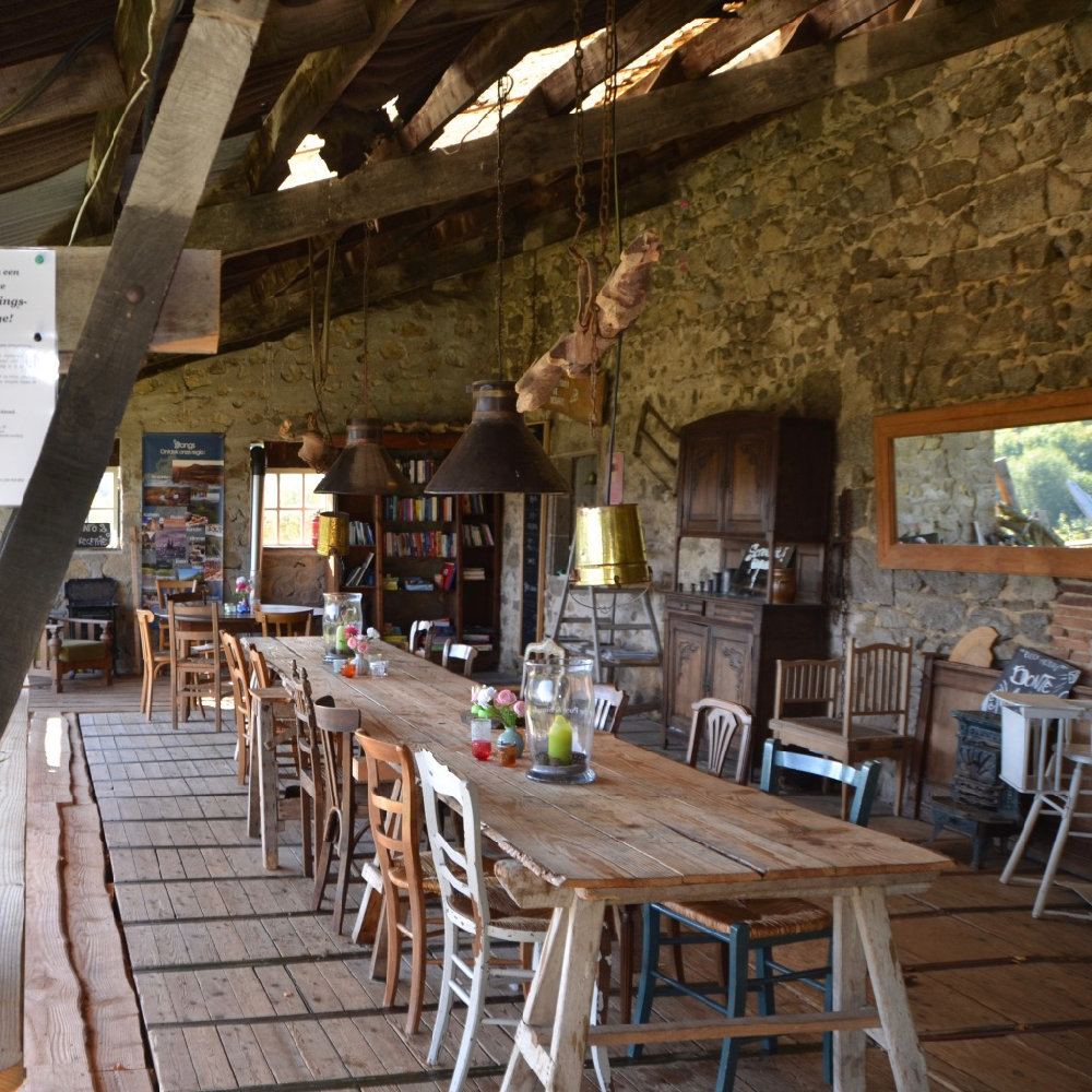 Lange tafel met verschillende stoelen, onder een overkapping