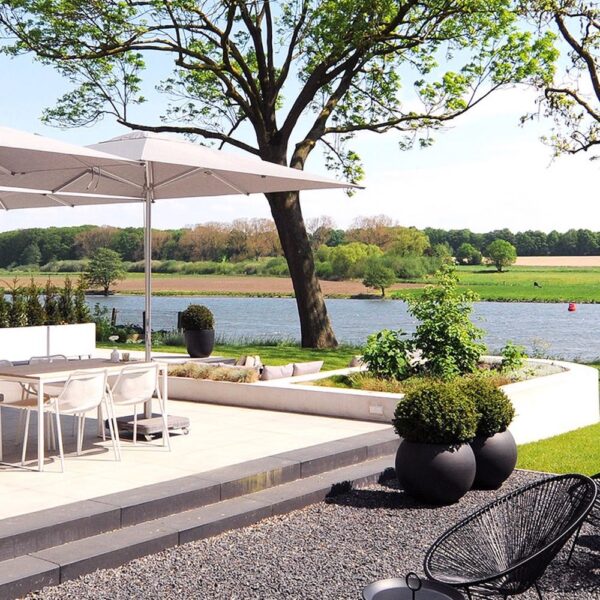 De tuin voor de gasten met loungehoek, eettafel met witte stoelen en zicht op de Maas