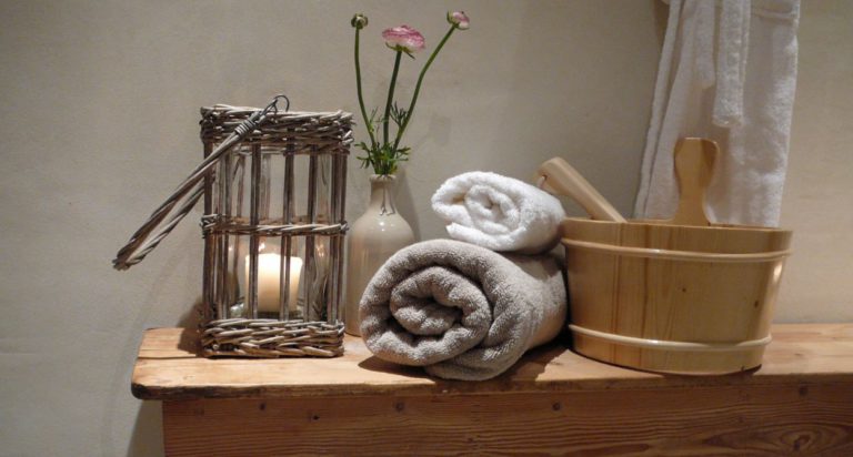 Sfeerbeeld voor sauna met kaarsje in sfeerlciht, handdoeken en houten waterbak met badjas