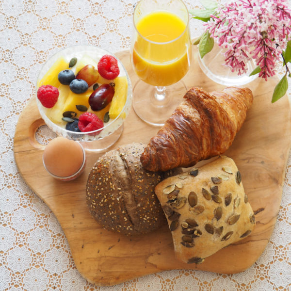 Een houten plank met ontbijtbroodjes, verse jus d'orange en fruit