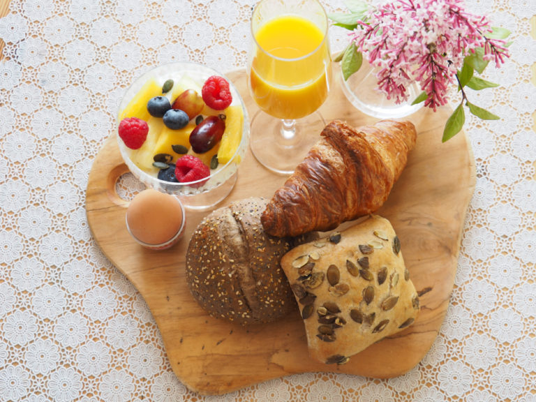 Een houten plank met ontbijtbroodjes, verse jus d'orange en fruit