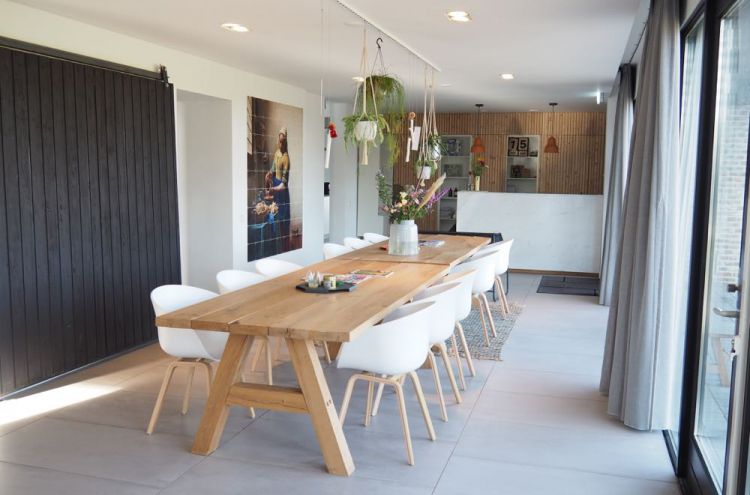 Een lange houten eettafel met witte kuipstoelen, grote bos bloemen en een IXXI met melkmeisje