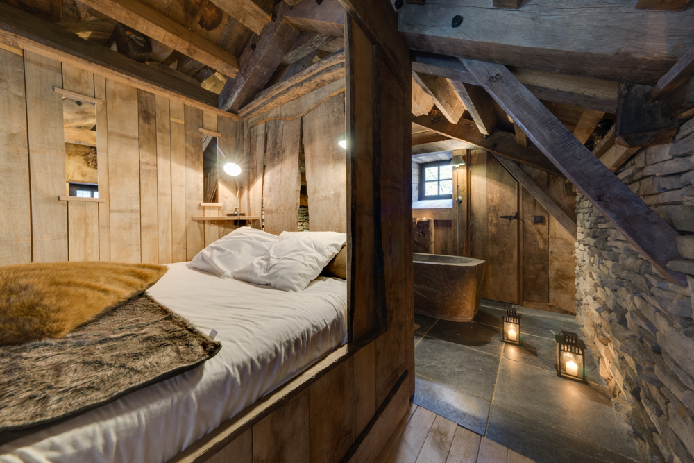 Een houten boomhut met tweepersoons bed, brandende kaarsen en een tobbe als bad