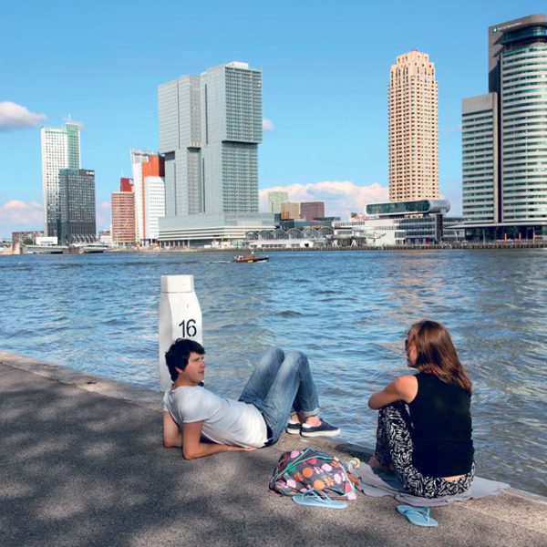 Twee jonge mensen op de kade met de skyline van Rotterdam op de achtergrond.