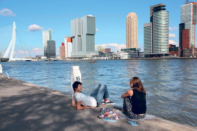 Twee jonge mensen op de kade met de skyline van Rotterdam op de achtergrond.