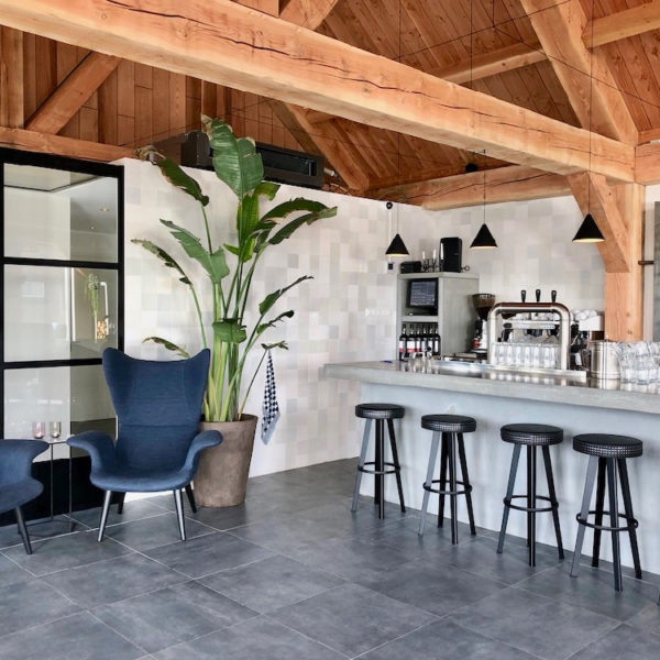 Betonnen bar, zwarte barkrukken, houten gebinten en blauwe fauteuils