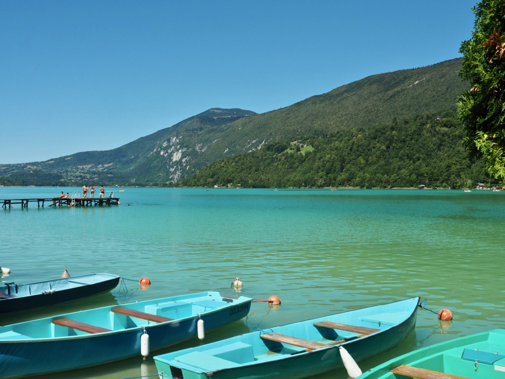 Groene en blauwe roeibootjes te huur. Op de achtergrond een steiger met zwemmende kinderen