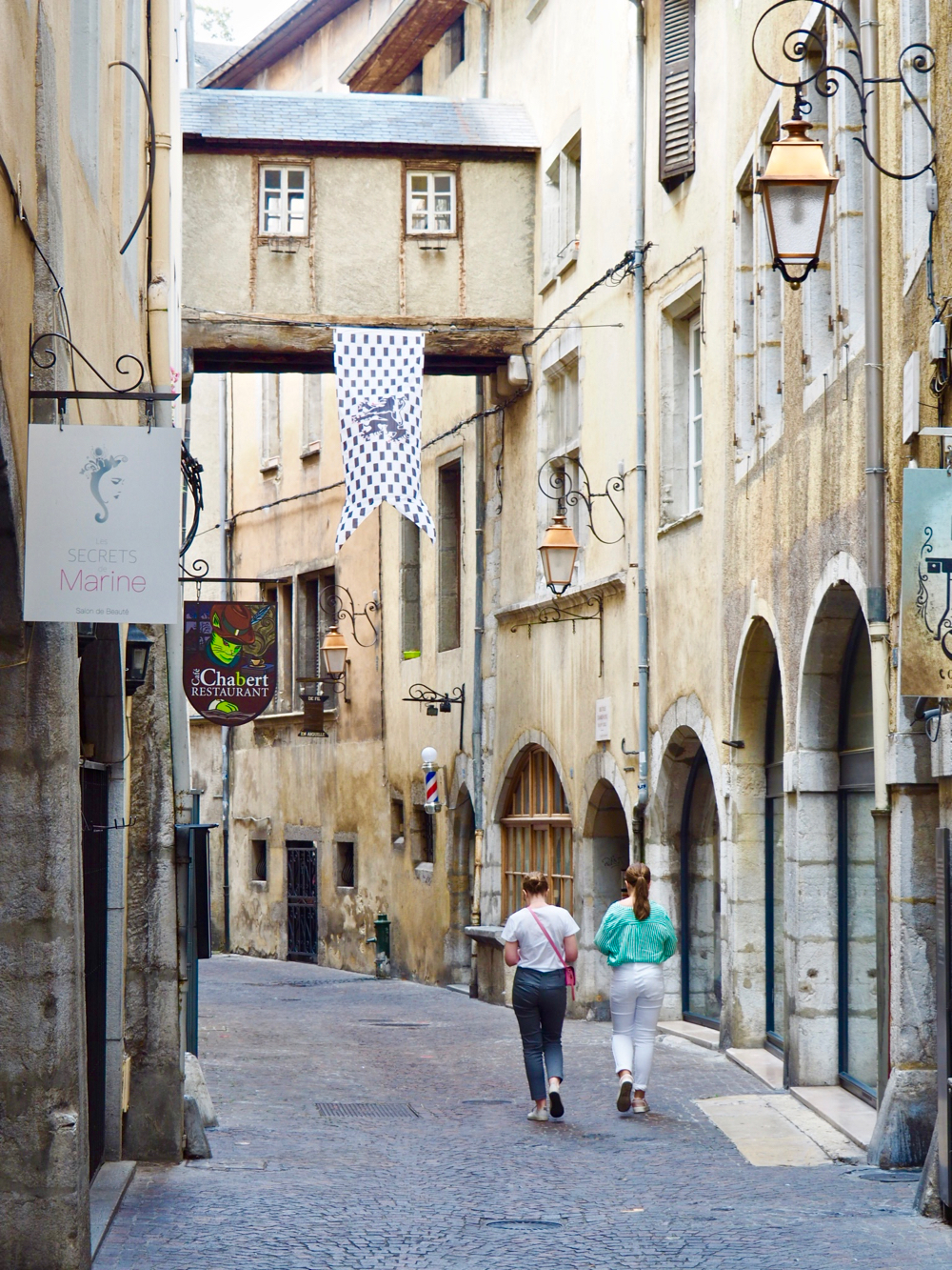 Een smalle straat met eeuwenoude zandkleurige huizen, waarvan enkele verbonden met een brug