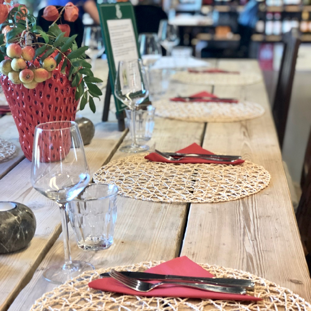 Een stoeren houten tafel met placemates, rode servetten en wijnglazen